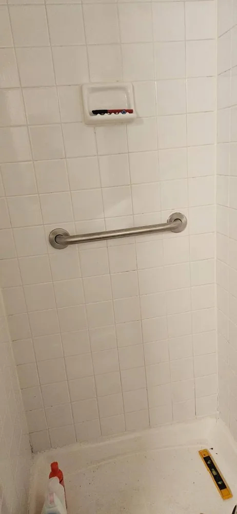 Stainless grab bar mounted on a white tiled shower wall
