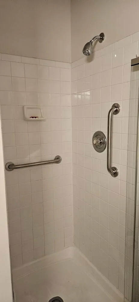 Two stainless grab bars mounted in a tiled shower beside the valve